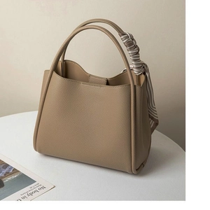 Khaki pebbled leather bucket tote bag with striped scarf handle on a white table