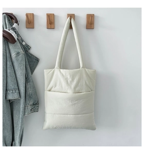 Quilted cream tote bag detail hanging on a hook next to a denim jacket and headphones