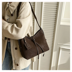 Detail of a dark brown matte leather tote bag featuring a Fashion metal tag and sleek strap