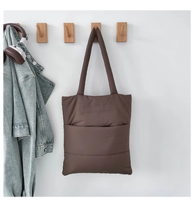 Detail of coffee brown quilted puffer tote bag on wooden hook with casual accessories