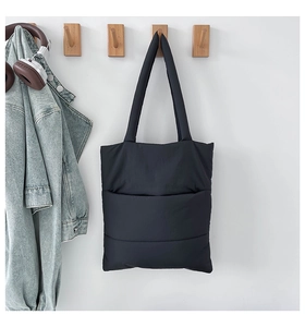 Detailed view of black quilted tote bag with front pocket hanging on a wooden hook
