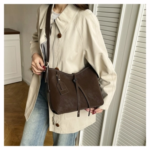 Close-up of a dark brown matte leather tote bag with long decorative straps and a tag