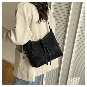 Detail of a black suede tote bag with decorative straps and a FASHION tag on the side