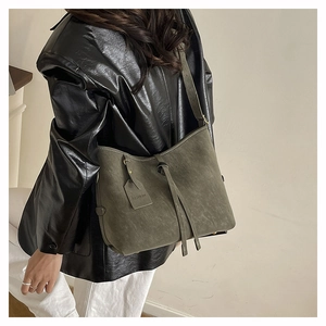 Detailed side view of a dark green matte leather tote bag worn with a black leather jacket
