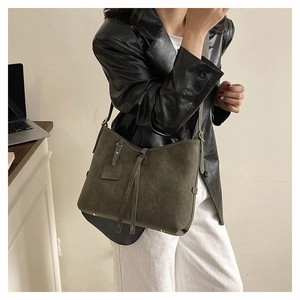 Detail of olive green suede tote bag with drawstring and embossed fashion tag on shoulder
