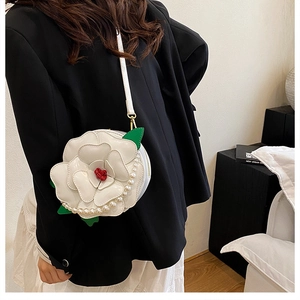 Detail of white 3D flower-shaped crossbody bag with pearl accents and green leaf decor