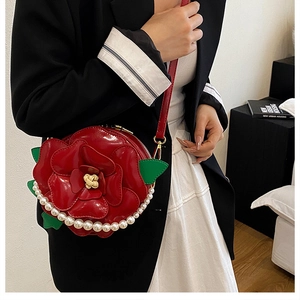 Detail of red rose-shaped crossbody bag with green leaves and pearl trim on model
