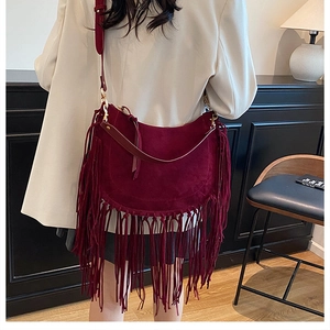 Detail view of a burgundy suede tassel tote bag worn by a model in a modern interior