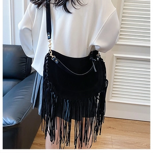 Detail of black suede fringe tote bag with gold hardware worn by a model in casual style