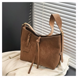Detail of a brown suede tote bag with leather strap and fashion tag on soft linen background