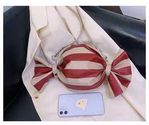 Detail of candy-shaped crossbody bag with red stripes and smartphone for size scale