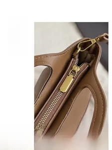Detail view of smooth golden zipper hardware and brown grain leather texture on tote bag