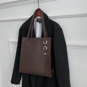 Detail of dark brown leather tote bag featuring a silver metal ring and buckle detail