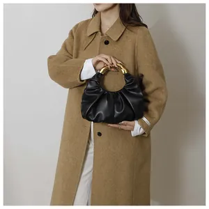 Detail of black pleated cloud bag with stylish chunky gold metal ring handle texture