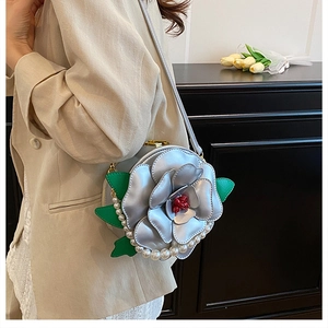 Detail view of silver camellia-shaped round bag with pearl trim and green leather leaves