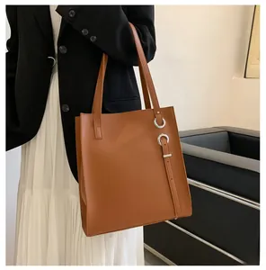 Close-up of caramel tote bag with silver ring buckle detail on model with black blazer