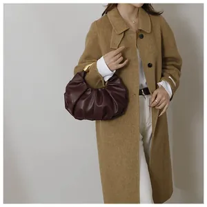 Detail of burgundy ruched cloud bag with golden metal handle and soft leather texture