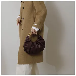 Detail of a dark brown pleated cloud handbag with elegant gold metal handle and leather texture