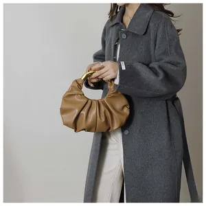 Close-up of brown pleated cloud bag featuring a curved gold metal handle held by model