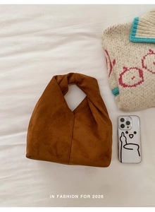 Detail shot of brown faux suede handbag with a twisted handle and triangle shape