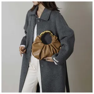 Detail of a brown pleated crescent bag featuring a luxury golden semi-circle metal handle