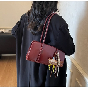 Détail du sac baguette en cuir verni bordeaux avec un charm ours en peluche sur l'anse