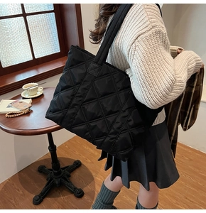 Detail of black quilted tote bag with diamond pattern shown in a cozy cafe setting