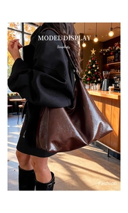 Detailed view of deep brown leather tote bag on model in a warm cafe interior setting
