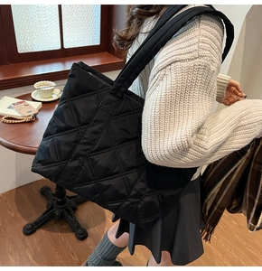 Detail of a black quilted nylon tote bag with large diamond stitching and wide strap