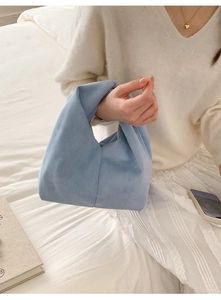 Detail of light blue suede handbag with knotted handle held by model in soft morning light