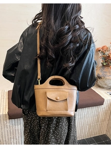Detail of a brown leather mini bucket bag worn crossbody with an adjustable shoulder strap