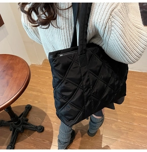 Side view of a large black quilted tote bag worn with a beige knit sweater in a cozy setting