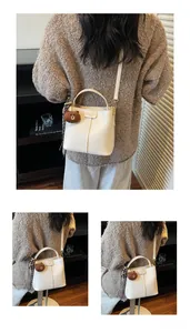 Close-up of beige textured bucket bag with decorative stitching and cute brown bear pendant
