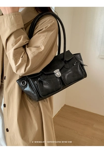 Detail of a black glossy leather shoulder bag with silver buckles on a trench coat model
