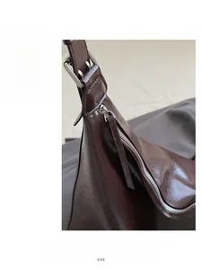 Detail of dark brown leather shoulder bag showing silver zipper and premium texture