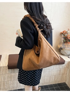 Detail of a large brown faux suede tote bag featuring a stylish pleated shoulder strap