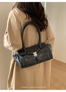 Detail of dark grey retro biker bag with silver buckles worn with a trench coat