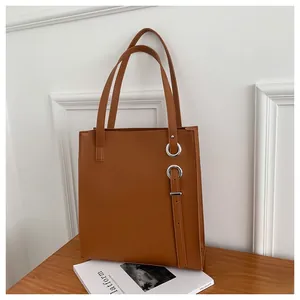 Detail of a brown leather tote bag with metal ring decoration on a wooden table