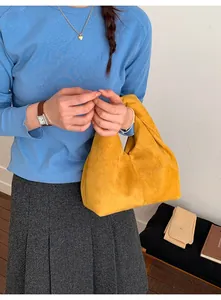 Detail of a ginger yellow pleated cloud handbag held by a model in casual style