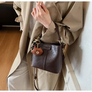 Detail view of dark brown bucket bag with plush bear charm and adjustable shoulder strap