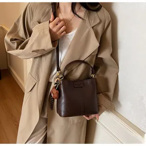 Detail view of deep brown bucket bag with plush bear charm and adjustable shoulder strap