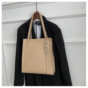 Close-up of light beige tote bag featuring silver metal rings and decorative straps on white wall