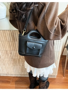 Back view of a black leather bucket bag worn by a model with a detachable strap