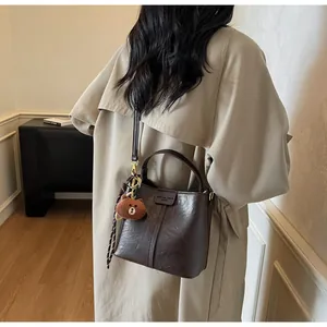 Detail of a dark brown vintage bucket bag with decorative stitching and plush bear charm