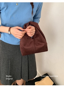 Detail of a dark brown velvet handbag shown with a pleated skirt for a retro aesthetic