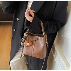 Detailed view of vintage brown leather bucket bag with vertical stitching and plush bear charm