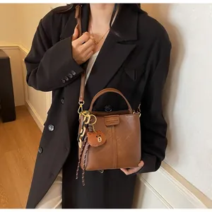 Detail of vintage brown bucket bag featuring a metal hook and plush bear charm