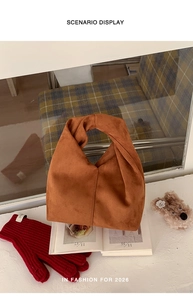 Brown suede handbag featuring an integrated twisted handle on top of a white table surface