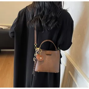 Brown vintage bucket bag with plush bear charm and striped scarf detail on model