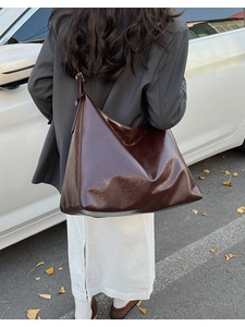 Deep brown glossy leather tote bag shown in use during a casual outdoor street scene